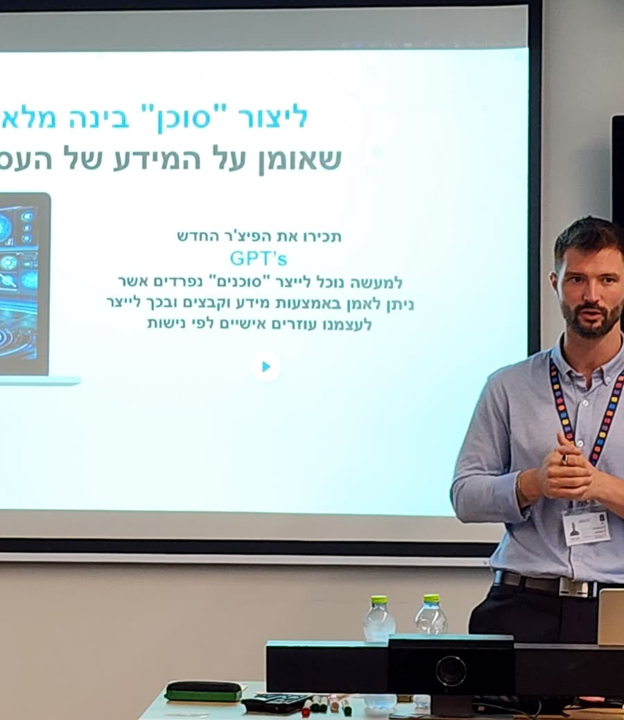 מקסים גומברג מעביר הדרכת סוכני AI בארגון, מול מסך עם שקופית ״ליצור סוכן בינה מלאכותית שאומן על המידע של העסק שלכם״